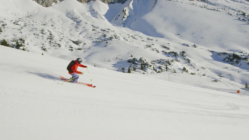 Skier with backpack skiing down hill near to mountain range at day