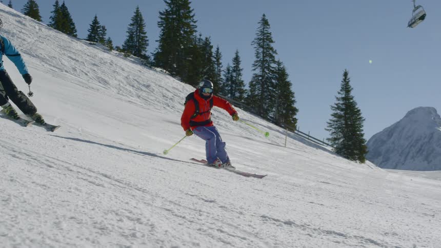 Two people slide down and around on the slope with their skis