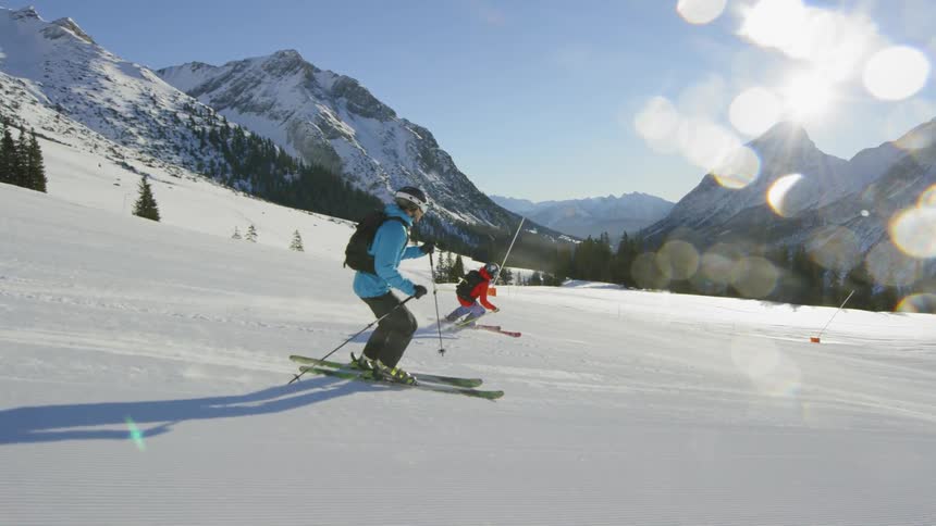 Skiers kick up snow as they make their way down a slope