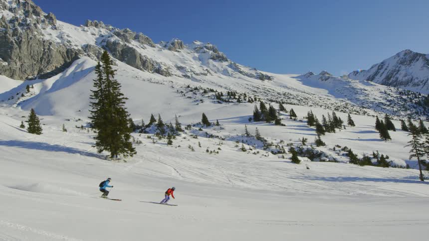 Two skiers make their way down a snow covered hill
