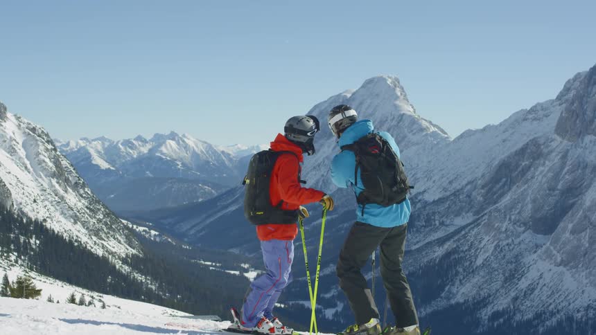 Two skiers take pictures of a snow covered mountain