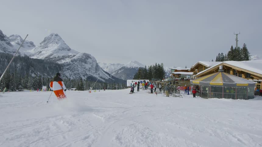 A skier skiing up to a crowd of skiers outside a ski lodge