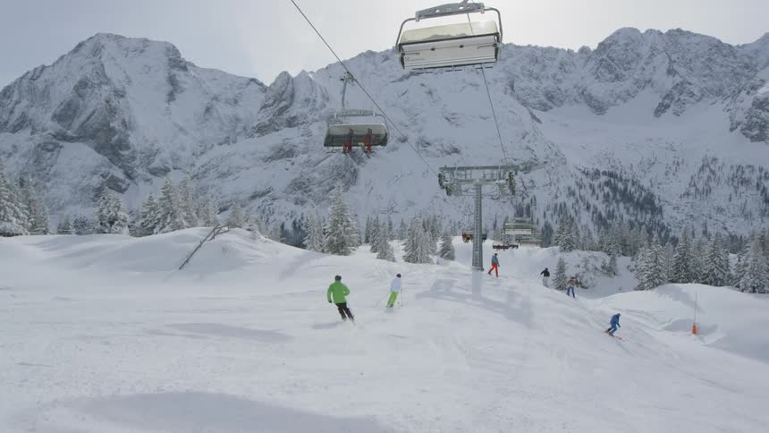 A ski lift passes above skiers going down a small slope