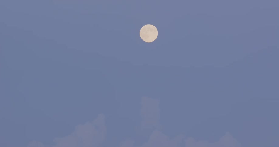 A full moon sits high in the sky as it is not quite dark outside