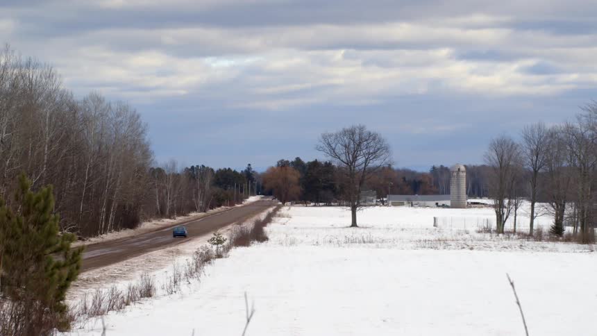 A car drives down a road next to a snow covered field