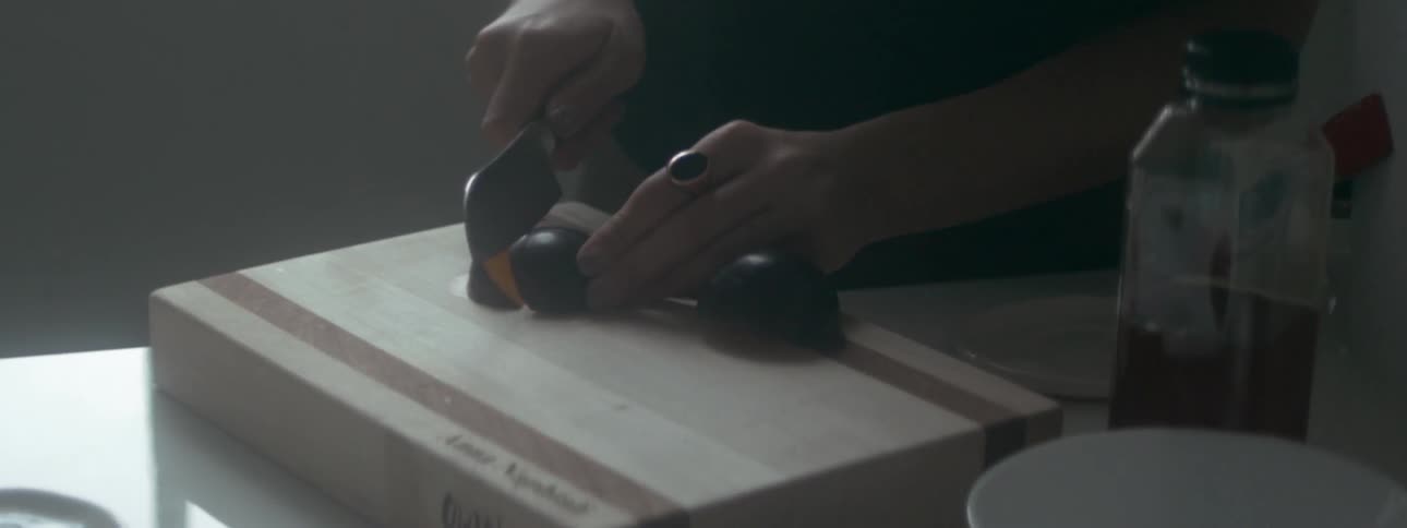 A woman slices a plum on a thick cutting board in a kitchen
