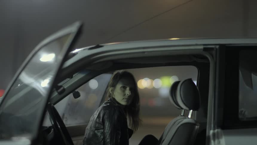 A woman in a leather jacket sits in a car and nods