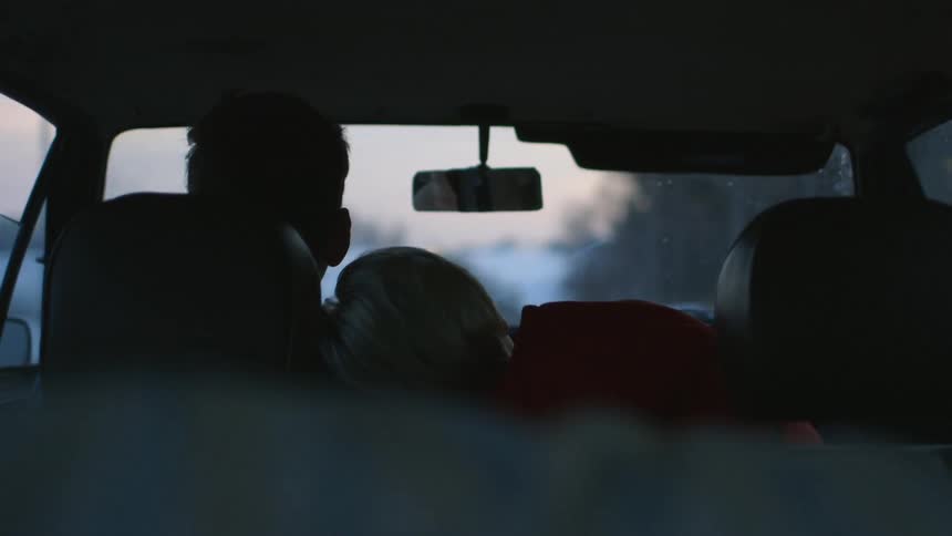 A person leaning against a driver in a car