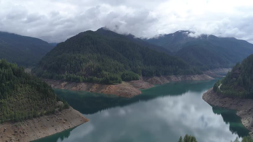 Clear lake water surrounded by tree covered hills and mountain ranges