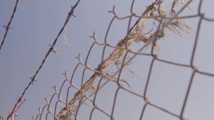 Barbed wire on top of wired fence in front of power lines