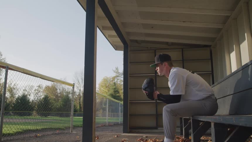 A man is holding a baseball glove and sitting on a bench