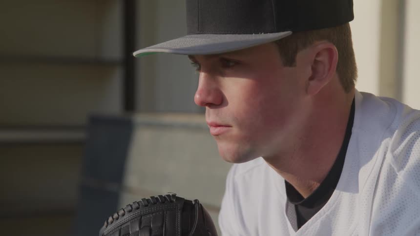 Baseball player wearing baseball cap sitting on bench waiting