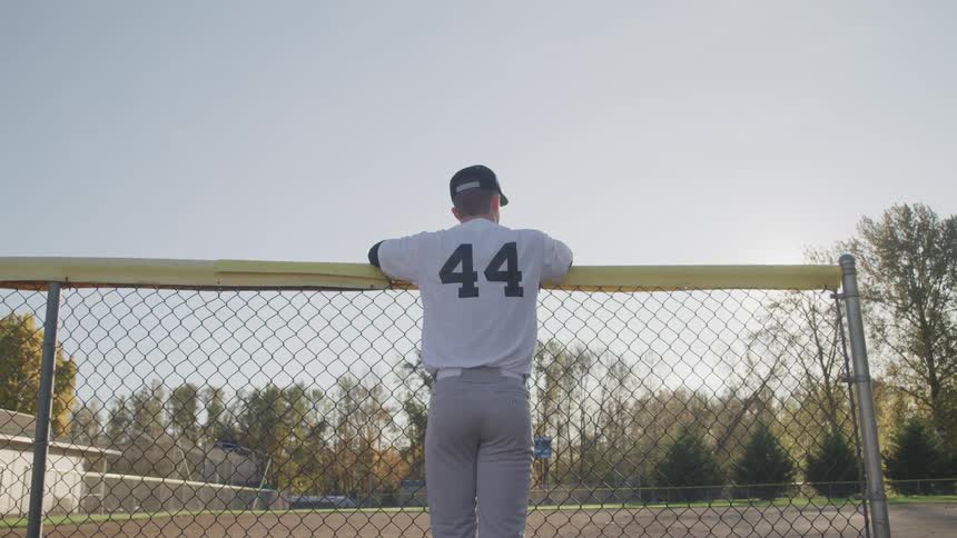 Baseball player rests his elbows on the banister and looks around in the baseball field