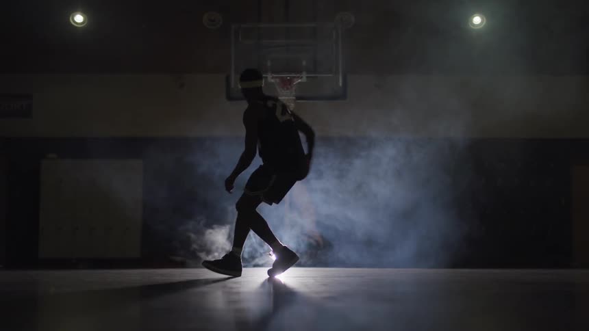 Black basketball player silhouette plays basketball in the spotlight in the basketball court