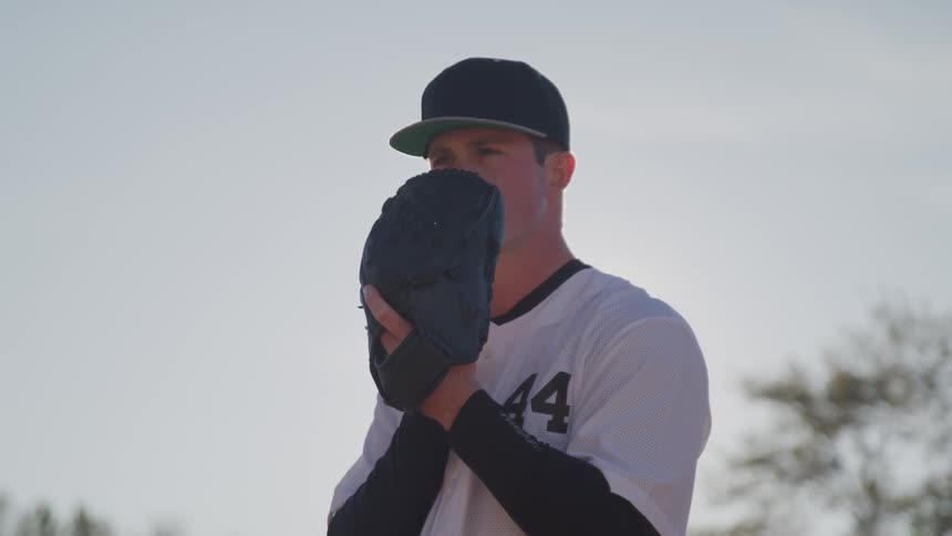 A baseball pitcher covers his mouth with his glove