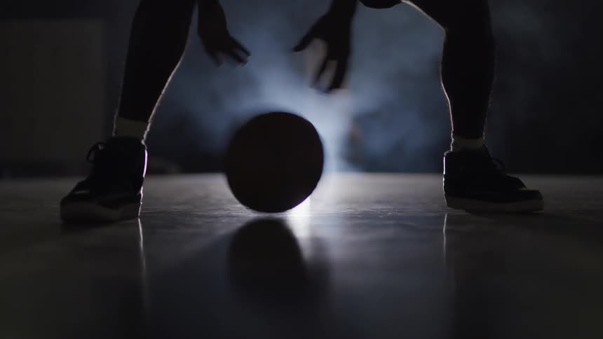 A basketball players legs spread out as he dribbles the ball low to the court