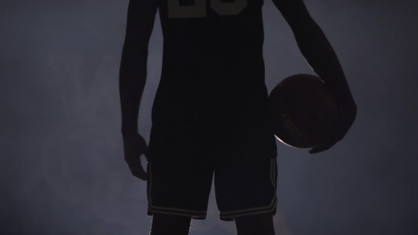 Black basketball players silhouette holds basketball in dark foggy basketball court