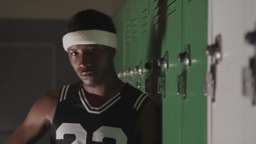Young black man in a white headband stands near the lockers and looks into the camera