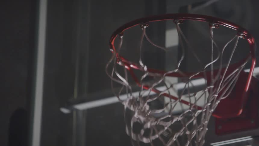 A basketball player slams the ball through the hoop with one hand