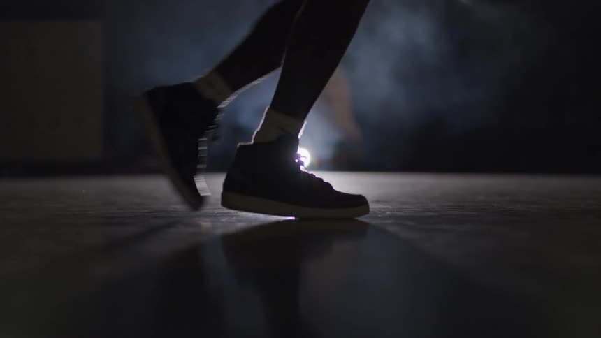 A man dribbles a basketball on a dark court lit by a flashlight laying on the floor