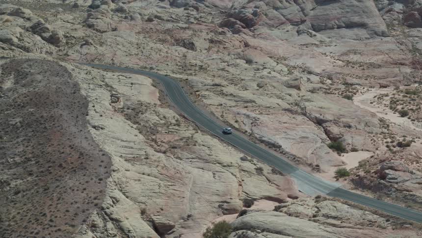 A car drives on a very windy road that runs through bare mountains