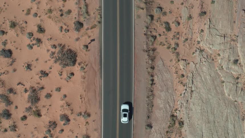 Aerial of white car driving on road in the desert