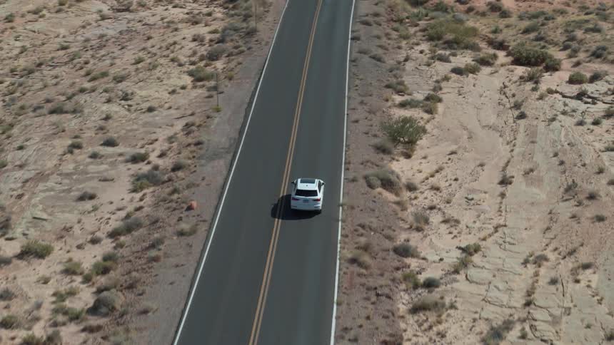 A white automobile drives down a lonely stretch of highway