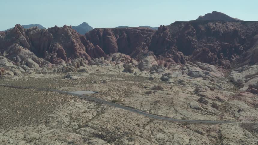 A car travels on an empty road with brush and rock formations