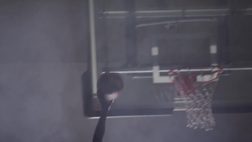 Two young men play basketball in a gymnasium and make a shot