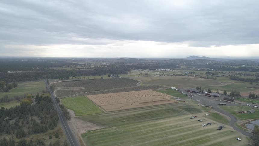 A farm with fields and equipment and a large brown wheat field with a design cut into it