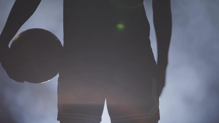 Black basketball players silhouette holds basketball in dark foggy basketball court