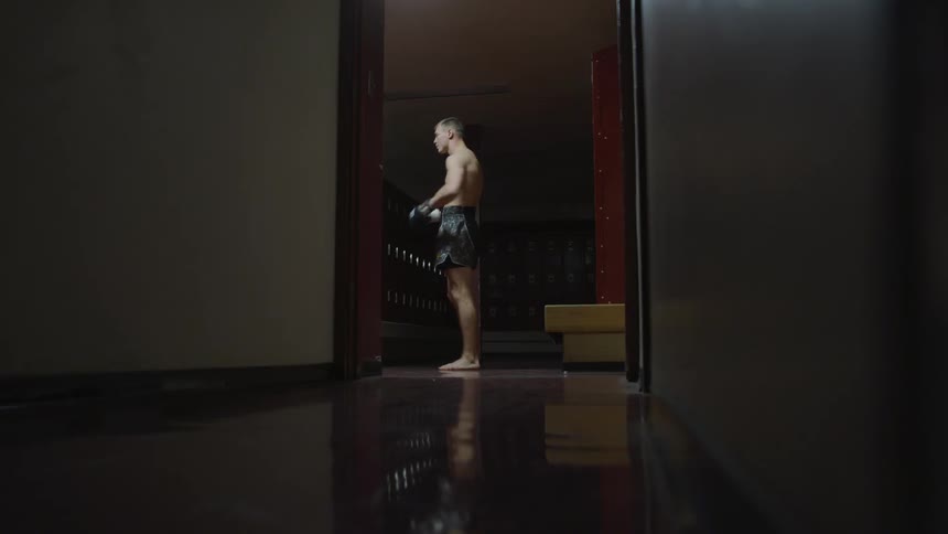 A man stands in a locker room jabbing the air to get ready for a fight