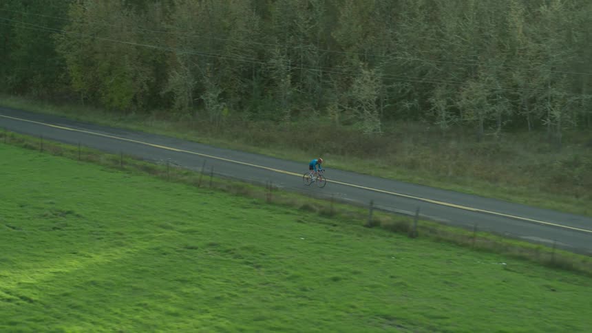 Man rides a bike along the asphalt road next to the forest
