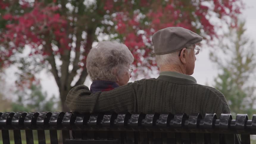 Senior man and woman sitting on the bench look sideways in the public park