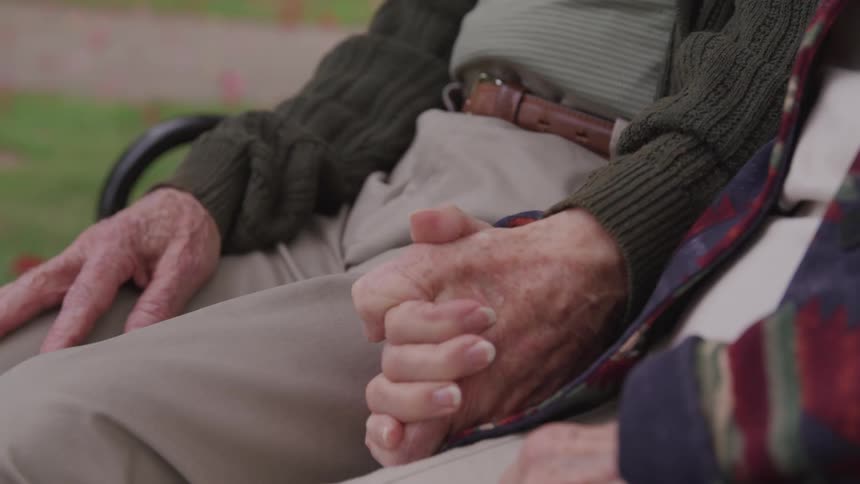 Senior old man and woman sitting on the bench hold hands in the public park