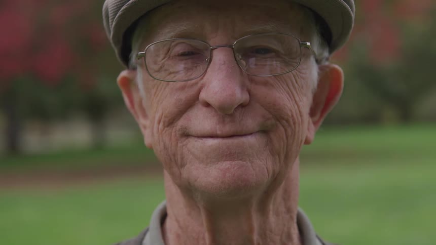 An old white man wearing a cap and glasses smiles