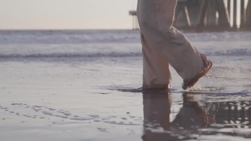 A person walks through the wet sand on a coast