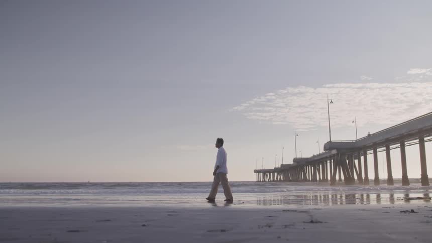 Man walking on the shoreline near the pier in early morning at the beach
