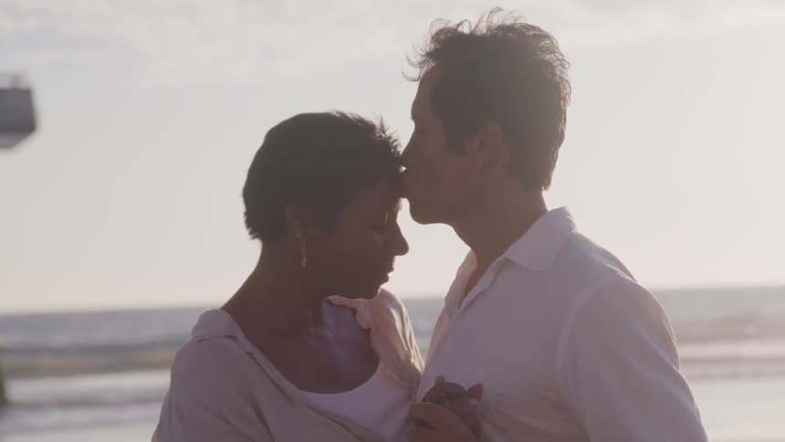 Husband kissing wife on forehead at the beach near the pier