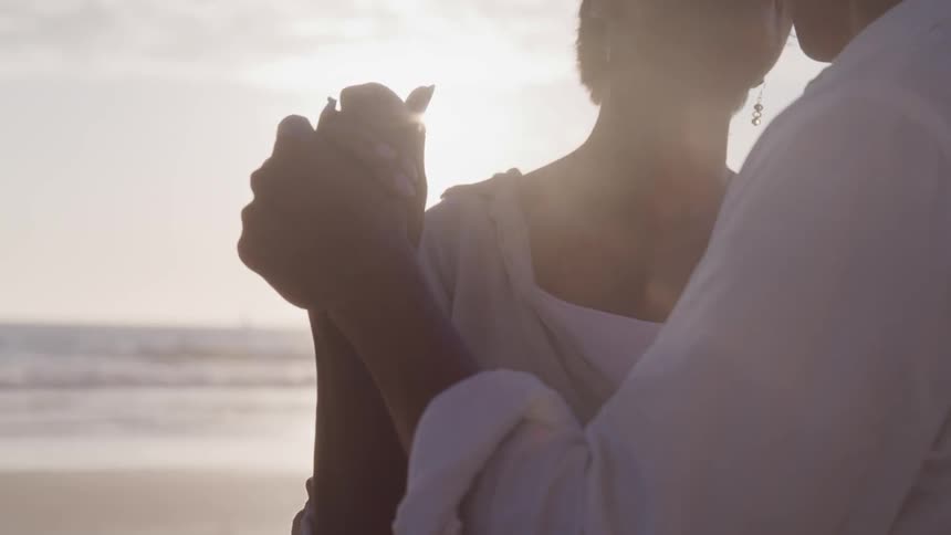 An old couple dancing at the beach under the sun flare