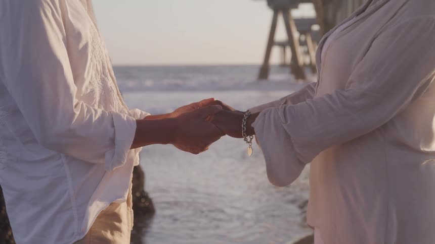 A man and woman holding hands under a pier on a beach