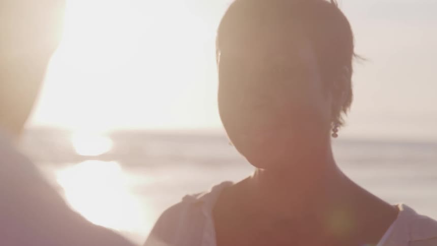 A woman looks lovingly at a man as they stand on the beach