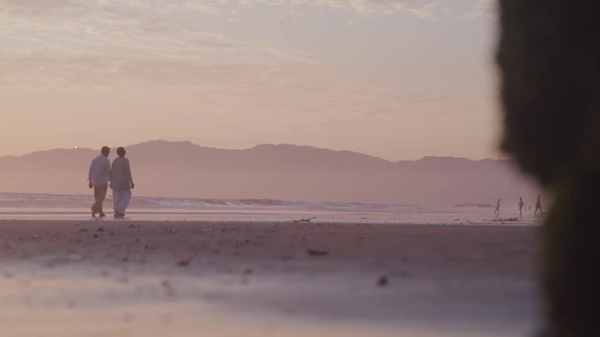 Couple hold hands and walks on beach next to ocean