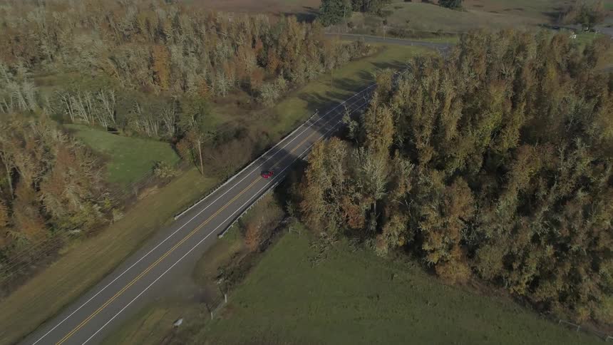 A red car drives down a rural highway
