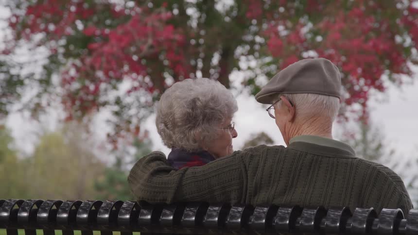 Elderly couple sitting on bench in park talking to each other