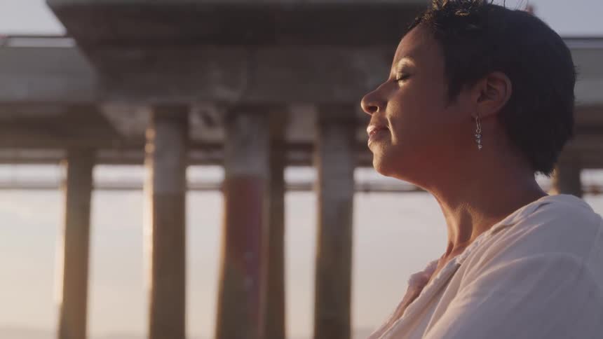 A woman stands with her eyes closed under a pier