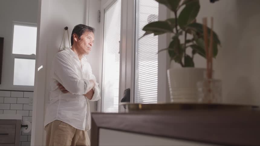 A man stands in a bathroom staring through the blinds of a door