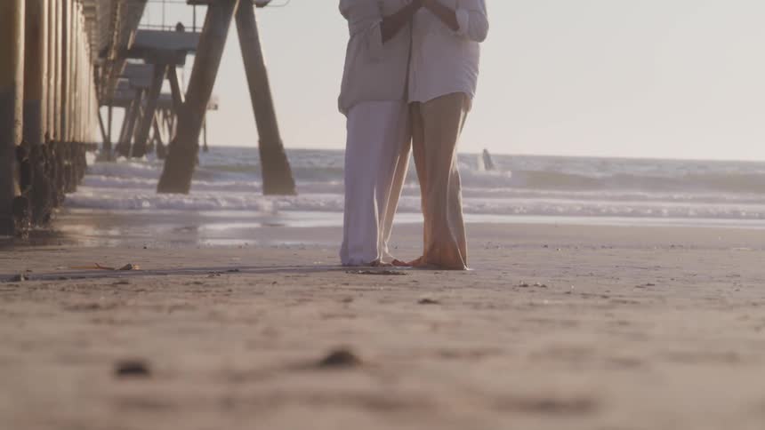 Couple hugging under pier on the beach next to ocean at sunset
