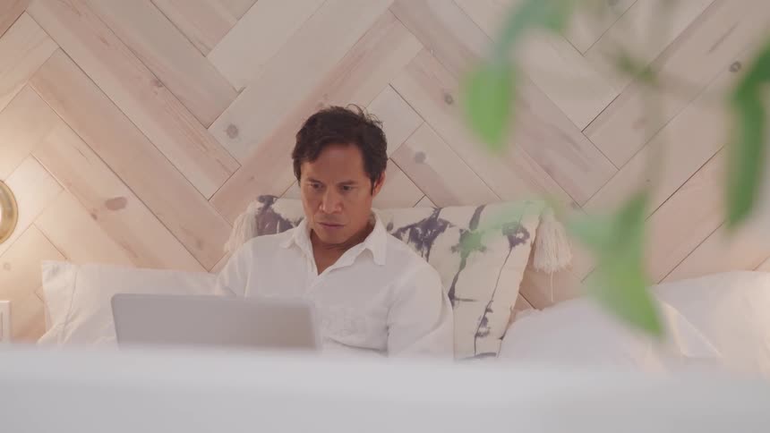 Man sitting in bed working on his laptop