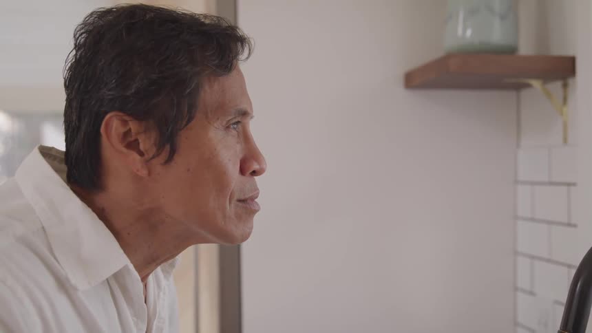 An elderly asian man looks contemplatively at a wall